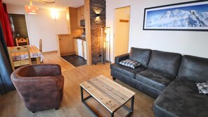 A cozy living room with a sofa, armchair, and coffee table, a kitchen area, and a dining table with chairs.