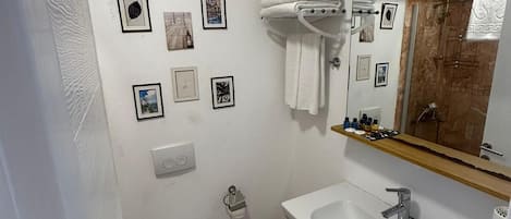 A bathroom with a toilet, sink, and mirror. There are several framed pictures on the wall.
