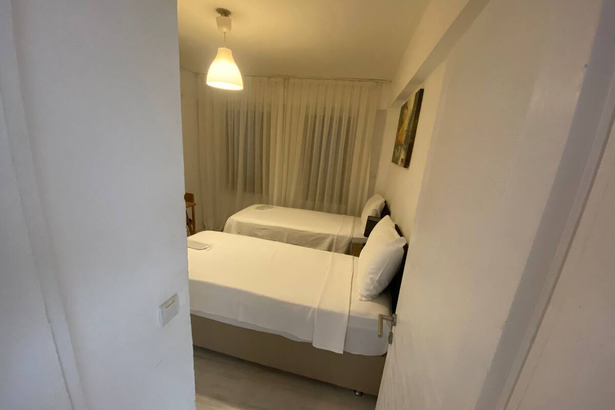 A room with two beds, a ceiling light, and a window with curtains.