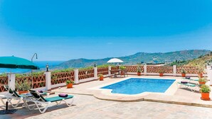 A rooftop pool with lounge chairs and umbrellas, surrounded by a wooden fence and potted plants, overlooking a mountainous landscape. - Casa Paqui in Frigiliana (Frigiliana)