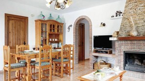 A dining area with a wooden table and chairs, a cabinet with glass doors, a fireplace, and a television. - Casa Paqui in Frigiliana (Frigiliana)