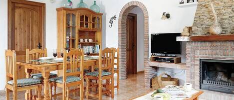 A dining area with a wooden table and chairs, a cabinet with glass doors, a fireplace, and a television.
