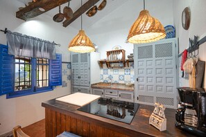 Una cocina con contraventanas azules, ollas de cobre colgando, una encimera de madera y una cafetera.