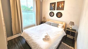 Ein Schlafzimmer mit einem großen Bett, einer Chandelier, einem Nachttisch mit Lampe und einem Fenster mit Vorhängen.