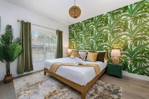 Ein Schlafzimmer mit einem Bett, einem Nachttisch, einer Lampe, einem Blumentopf und einem Fenster mit Vorhängen.