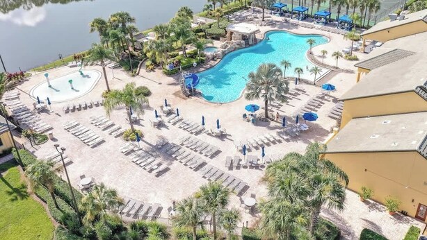 A resort with a large swimming pool, sun loungers, and palm trees. - Disney Retreat: Pool, Themed Rooms, Pets Welcome! (Kissimmee)