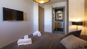 Een hotelkamer met een bed, een aan de muur bevestigde televisie, een spiegel en een badkamer die door een open deur zichtbaar is.