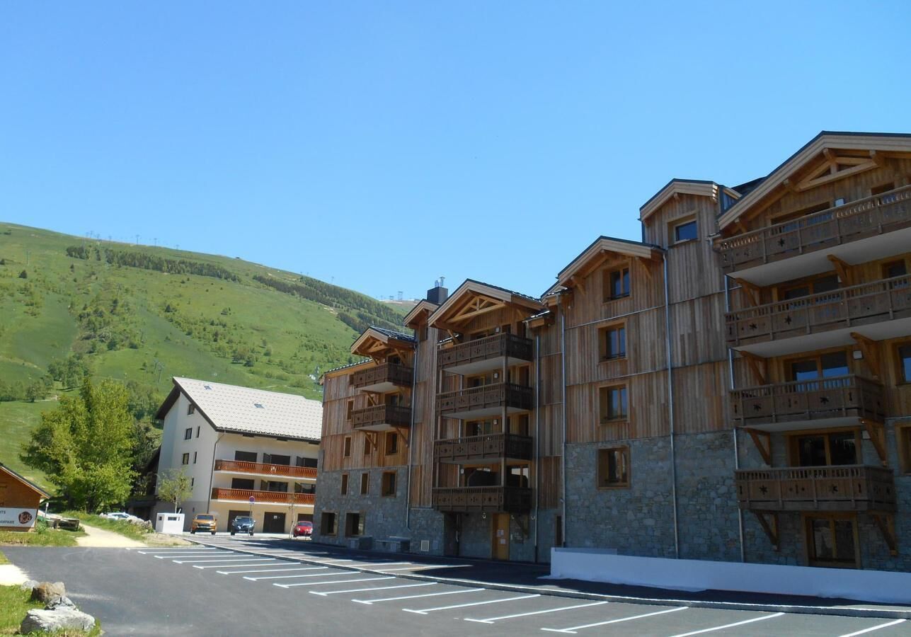Um hotel com vários andares, varandas, estacionamento e montanhas ao fundo.
