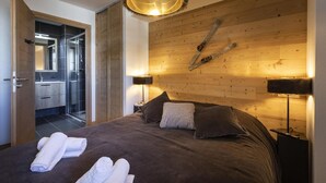 Ein modernes Schlafzimmer mit einem großen Bett, einem Holz-Kopfteil und einer Duschkabine aus Glas.