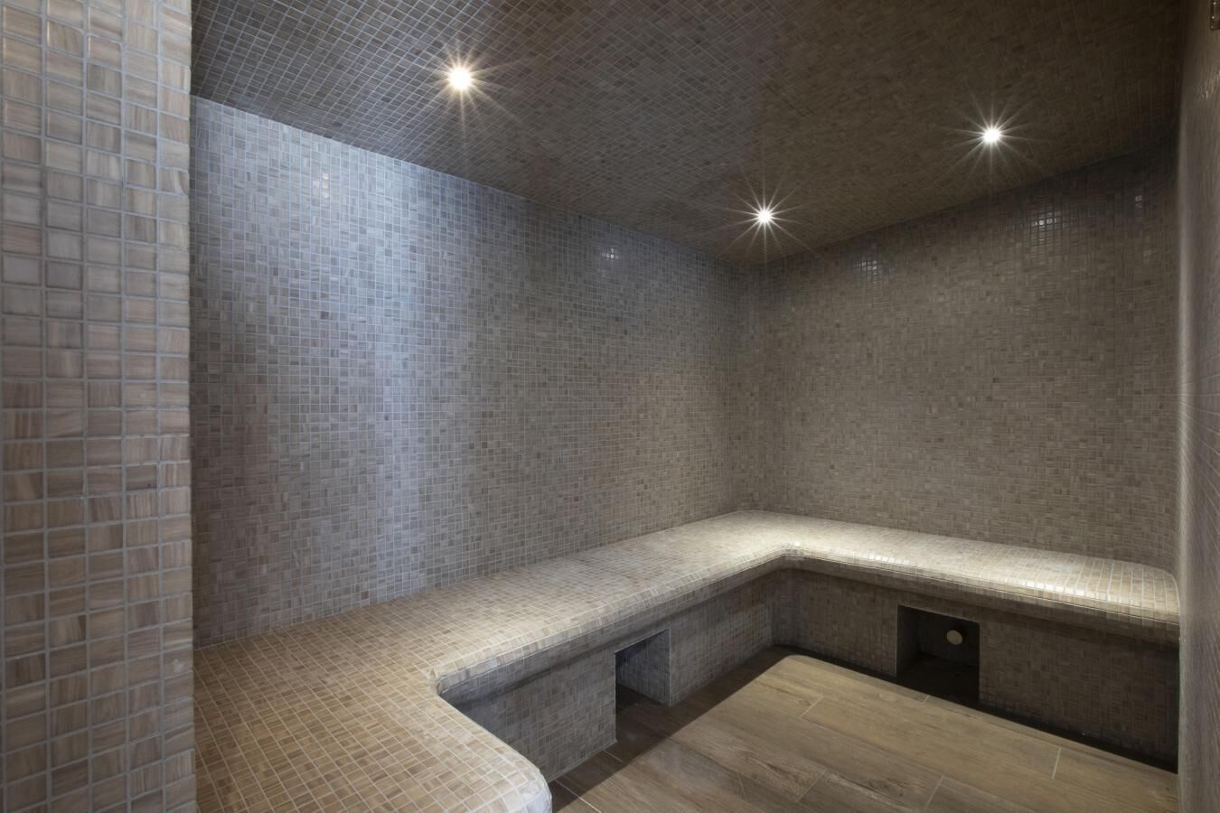 A spa room with a bench, tiled walls, and a wooden floor.