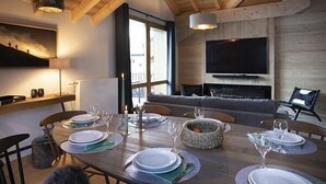 En matplats med ett träbord för fyra personer, en soffa och en tv som är monterad på väggen.