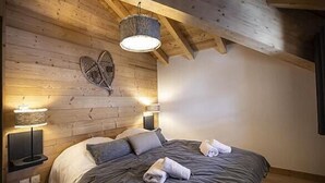 Ett mysigt sovrum med ett träpanelat tak, en säng med grå sängkläder, två sänglampor och en hjärtformad väggdekoration.