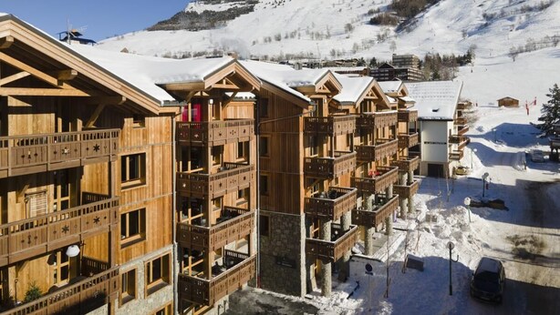 Een rij houten chalets met balkons, met een besneeuwd berglandschap op de achtergrond.