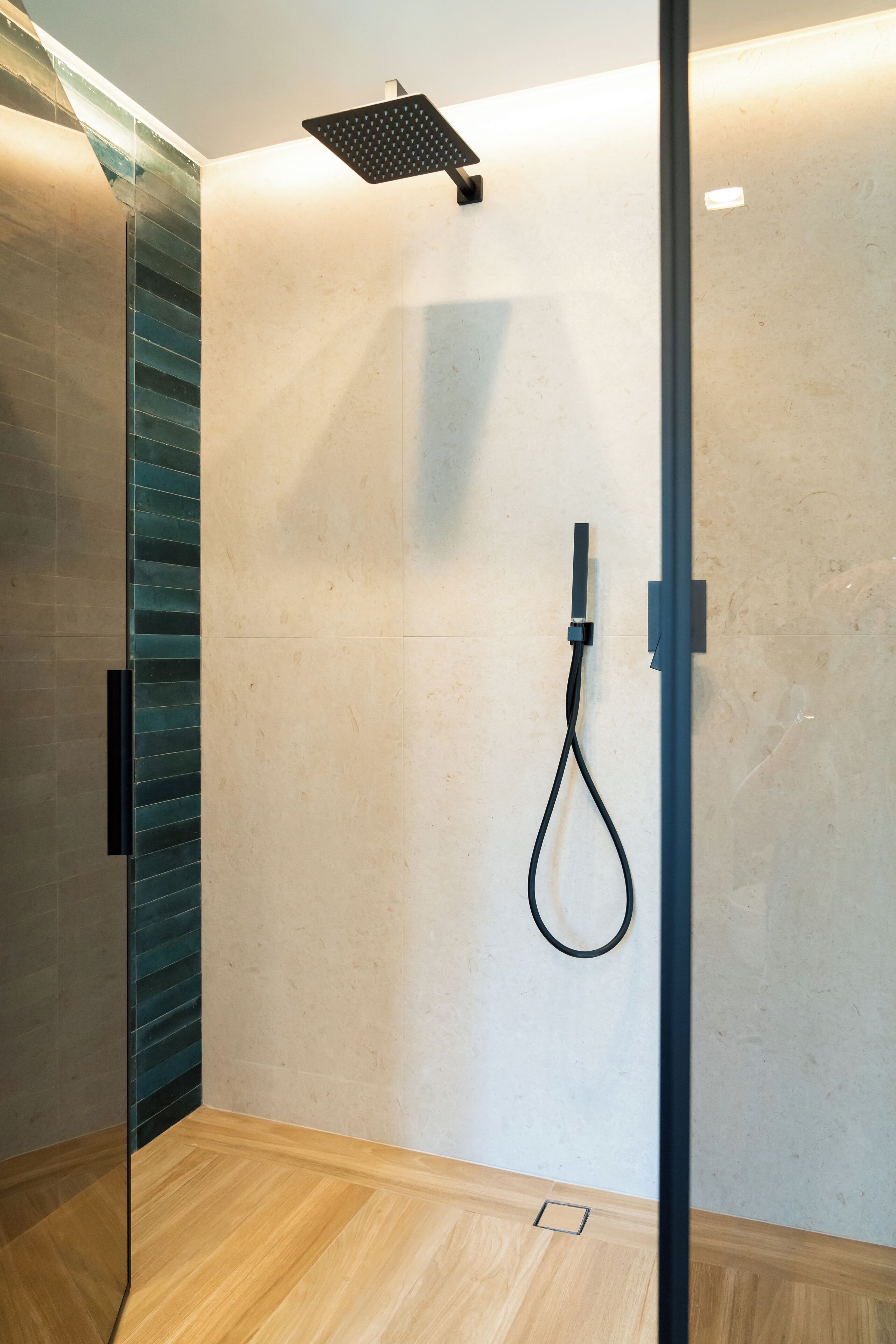 A modern shower area with a glass door, a wooden floor, and a wall-mounted showerhead.