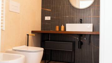 Een moderne badkamer met een houten wastafelmeubel, een ronde spiegel en twee witte toiletten.
