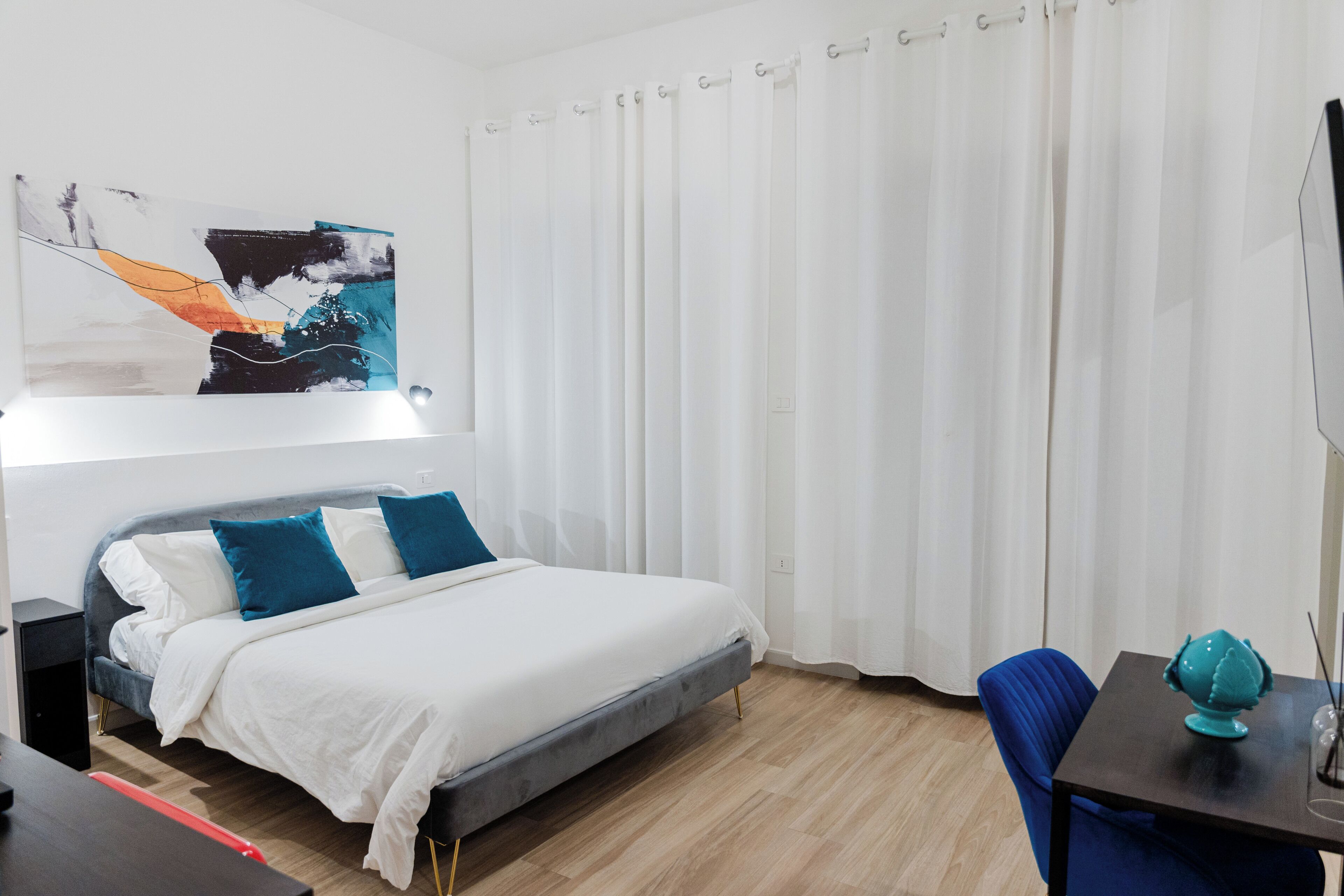 Et moderne hotelværelse med en seng, et skrivebord, en stol og et stort abstrakt maleri på væggen.