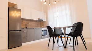 A modern kitchen with a stainless steel refrigerator, grey cabinets, a built-in oven, and a dining area with two black chairs.