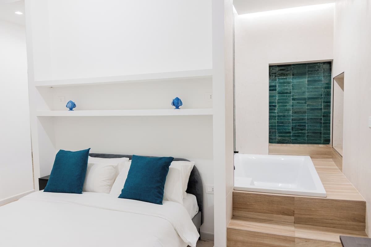 Un dormitorio moderno con una cama, dos almohadas azules, un cabecero blanco y un estante empotrado con objetos decorativos.