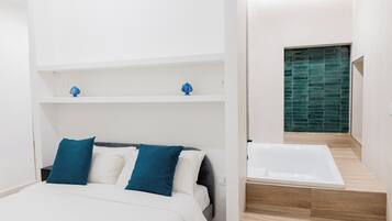 A modern bedroom with a bed, two blue pillows, a white headboard, and a built-in shelf with decorative items.