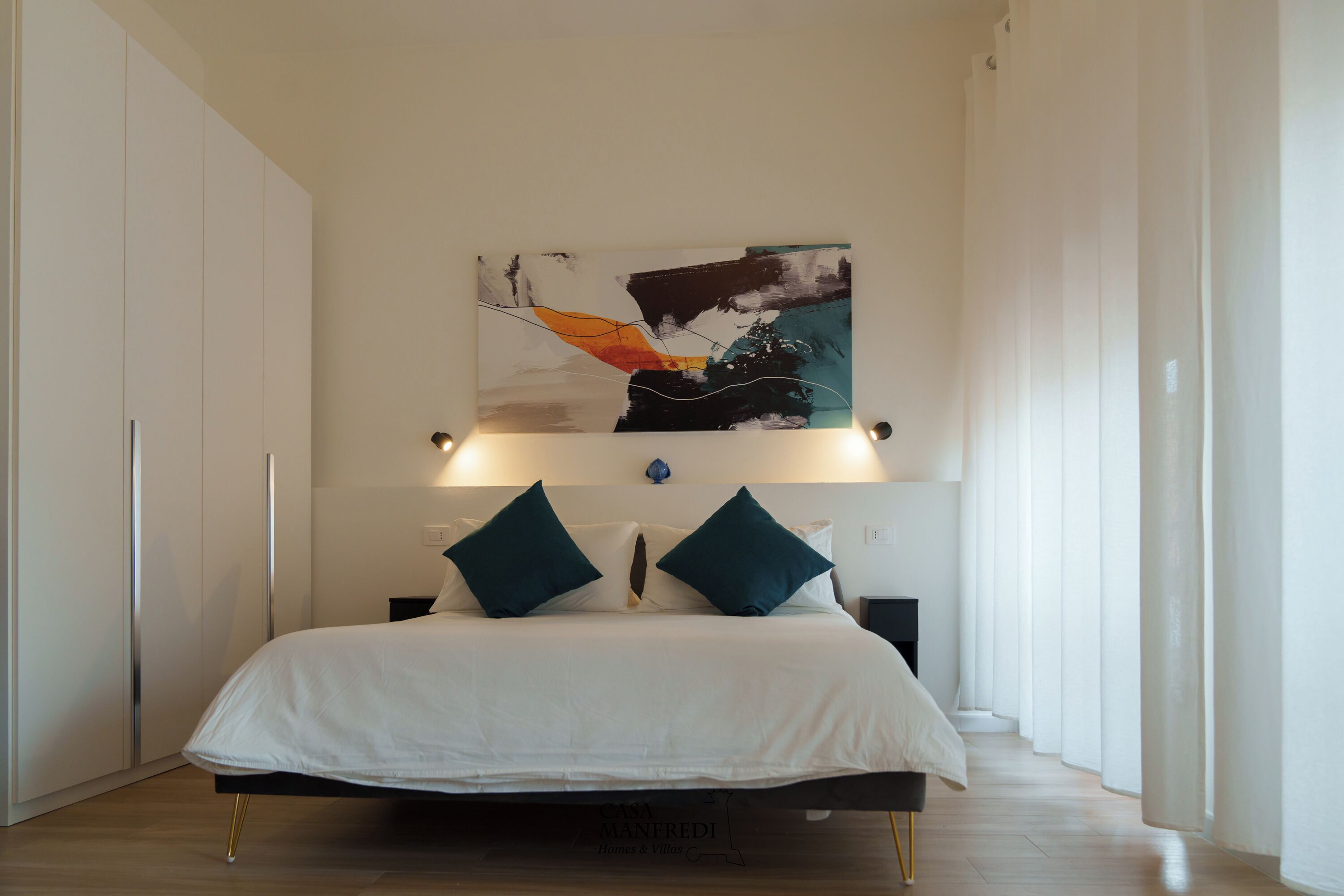 A modern bedroom with a bed, two pillows, a wall-mounted abstract painting, and a bedside table.