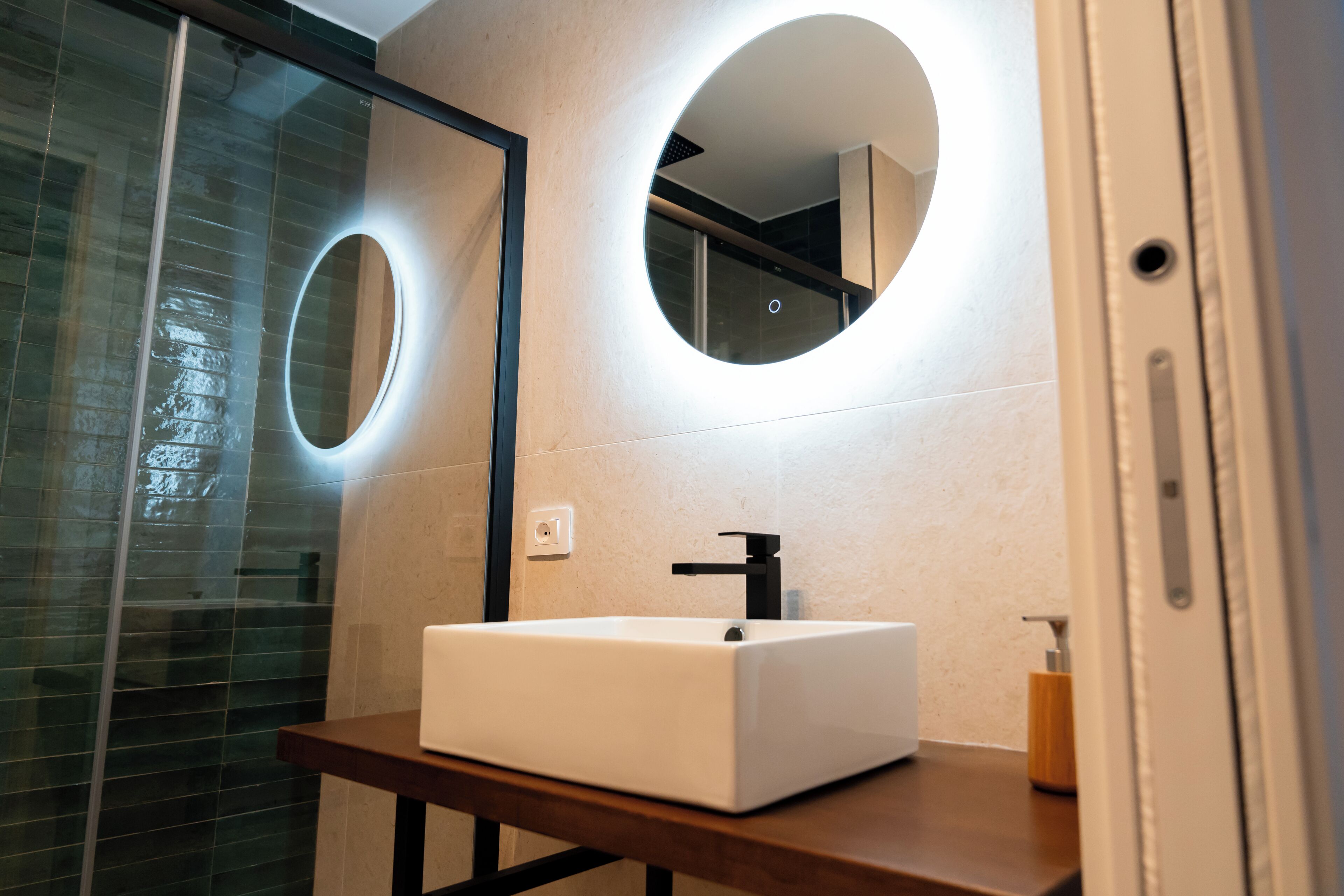 Une salle de bain avec un lavabo blanc, un miroir à cadre rond et une cabine de douche en verre.