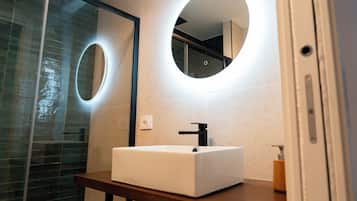 Une salle de bain avec un lavabo blanc, un miroir à cadre rond et une cabine de douche en verre.