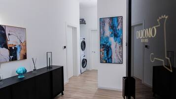 A hallway with a black console table, a large abstract painting, a washing machine, and a sign reading "DUOMO ROOMS".