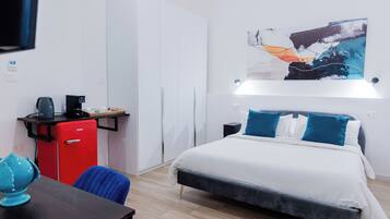 Une chambre d’hôtel moderne équipée d’un lit, d’un bureau avec un mini-réfrigérateur rouge, d’une machine à café et d’une chaise bleue.