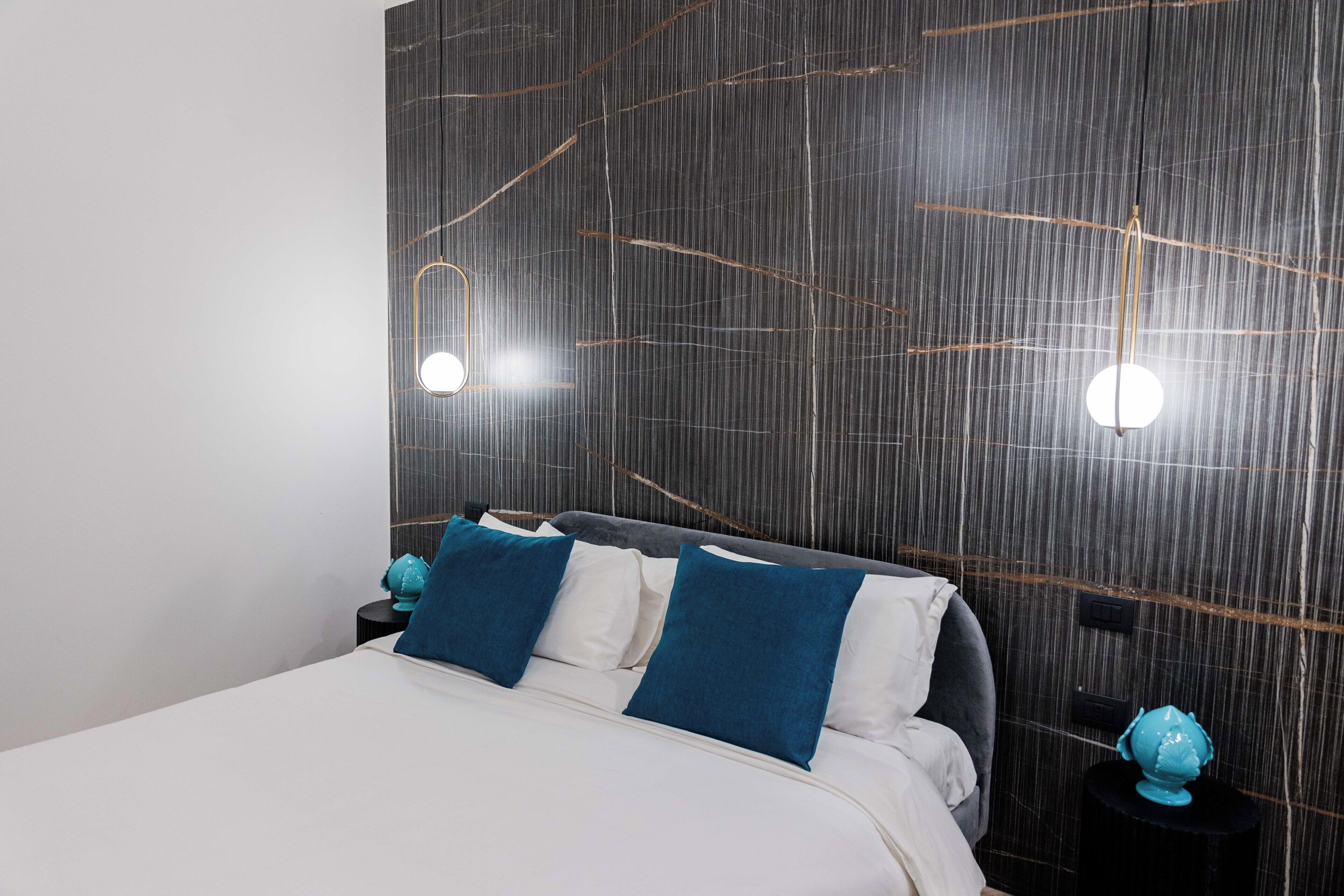 A modern bedroom with a large bed, two bedside tables with decorative globes, and a wall with a unique textured design.