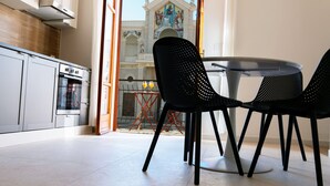 A modern kitchen with white cabinets, a built-in oven, and a dining area with two black chairs and a round table.