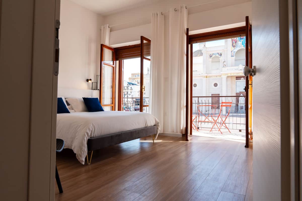 Un dormitorio con cama, vistas a la calle y un balcón con sillas.