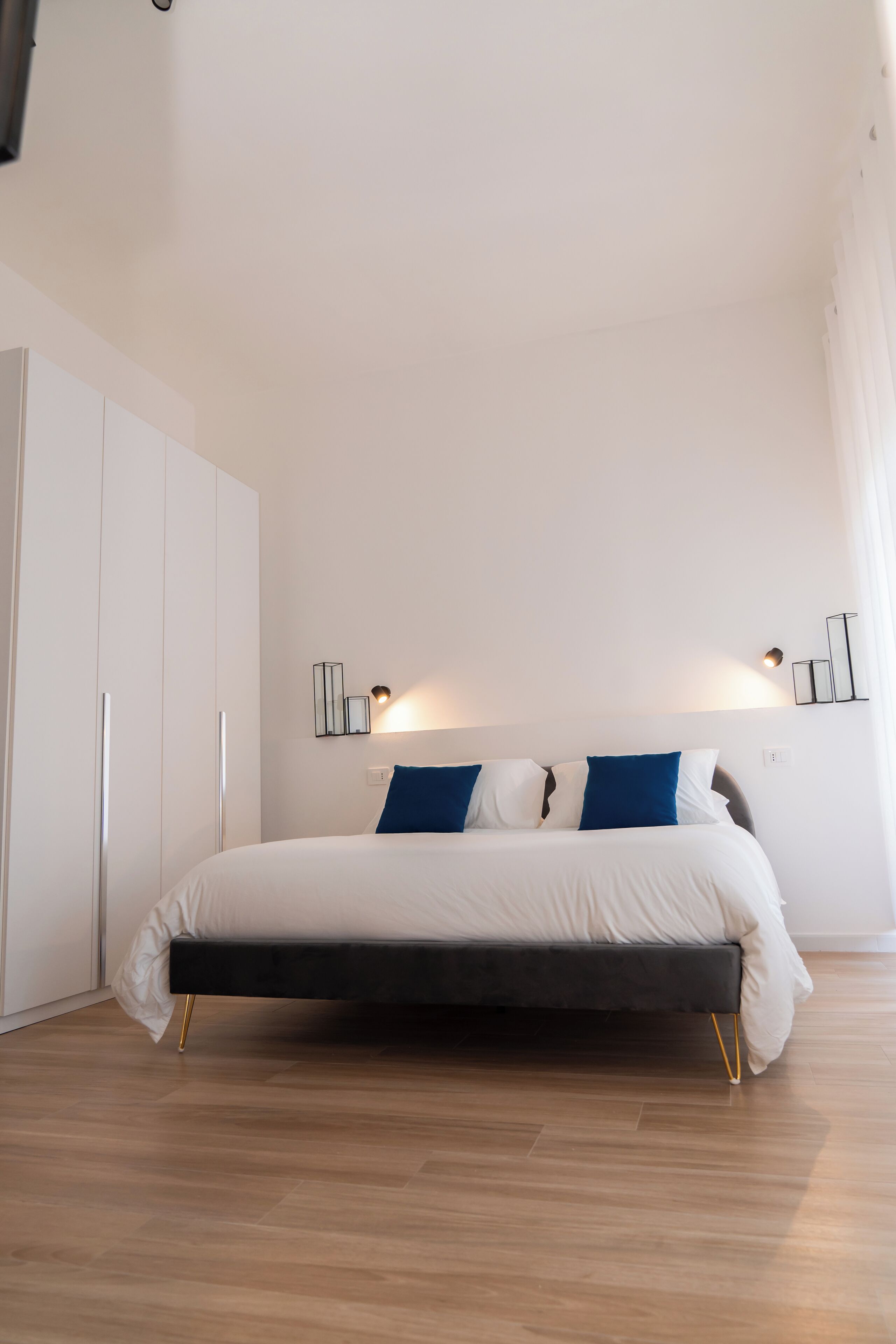 A bedroom with a bed, white wardrobe, and wall-mounted light fixtures.