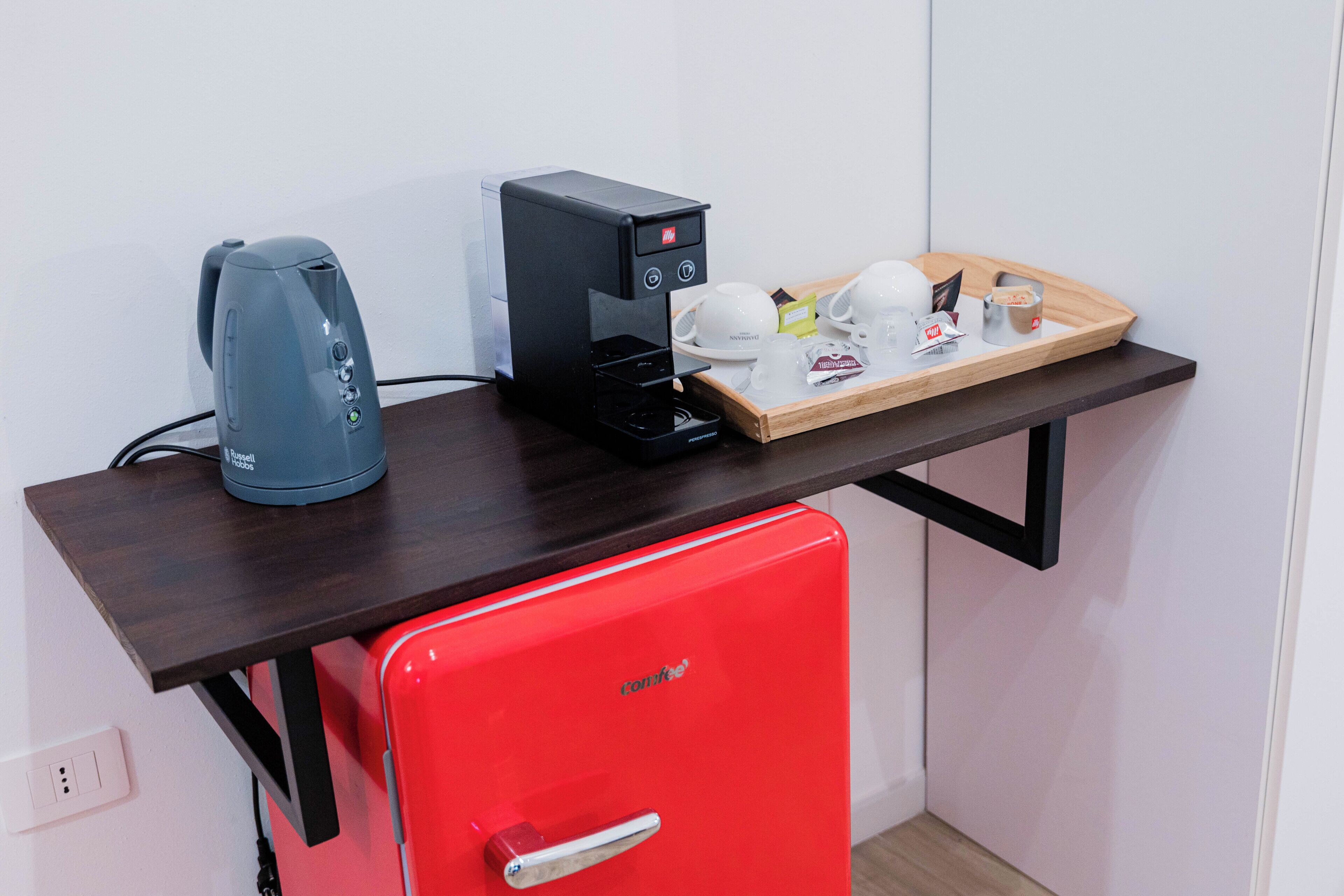 A compact kitchenette with a red refrigerator, a coffee maker, a toaster, and a tray with cups and condiments.