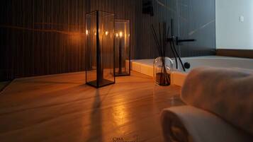 Ein modernes Badezimmer mit Holzboden, einer Badewanne mit Glasplatte und einer Glasvase mit Schilf.
