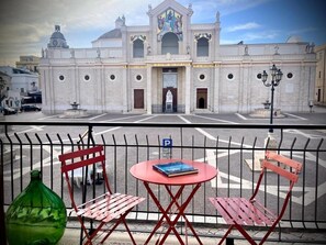 A historic building with a central dome and arched windows, a fountain in the courtyard, and a red metal fence with a table and chairs in the foreground.