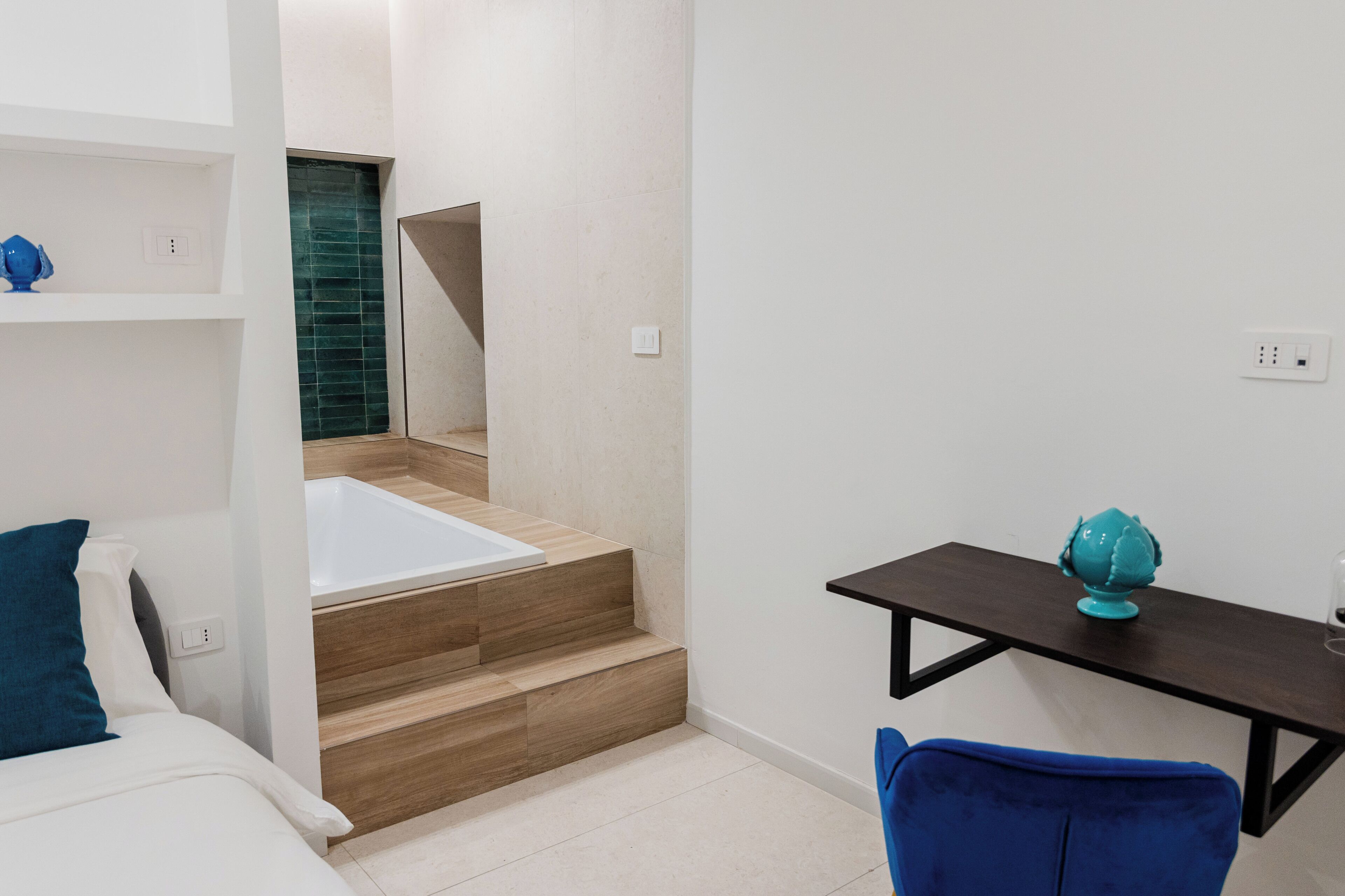 Moderni hotellihuone, jossa on puinen portaikko, joka johtaa kylpyhuoneeseen, pieni työpöytä, jossa on maapallo, ja sänky, jossa on siniset tyynyt.