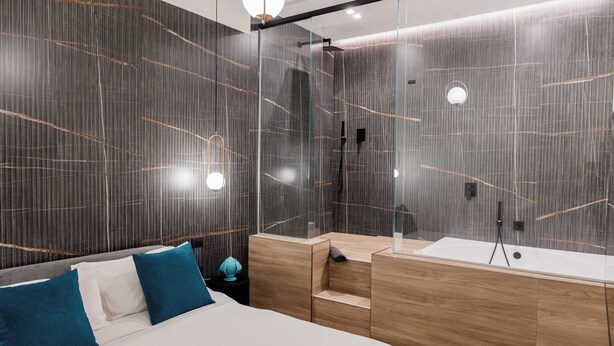 A modern hotel room with a large bed, a wooden vanity, and a glass shower enclosure.