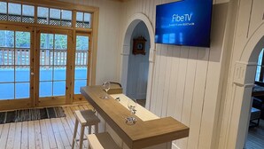 Een kamer met houten lambrisering, een lange tafel, twee krukken, een flatscreen televisie aan de muur en grote ramen met uitzicht op het landschap.