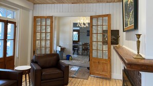 Een kamer met houten lambrisering, een bruine leren bank, een houten eettafel met stoelen en een kroonluchter.