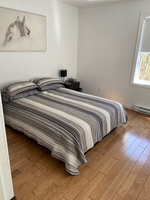 Un dormitorio con una cama, una mesita de noche, una lámpara y una ventana.