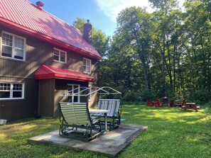Ein zweistöckiges Haus mit rotem Dach und überdachter Terrasse, komplett mit Tisch und Stühlen.