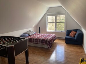 Ein Zimmer mit einem Kicker, einem Bett mit karierter Bettdecke, einem blauen Sofa und einem Fenster mit Blick auf Bäume.