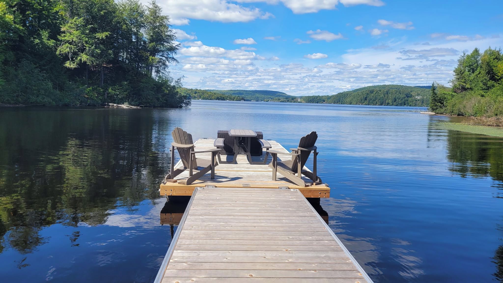 A wooden dock extending into calm water with a picnic table and chairs.