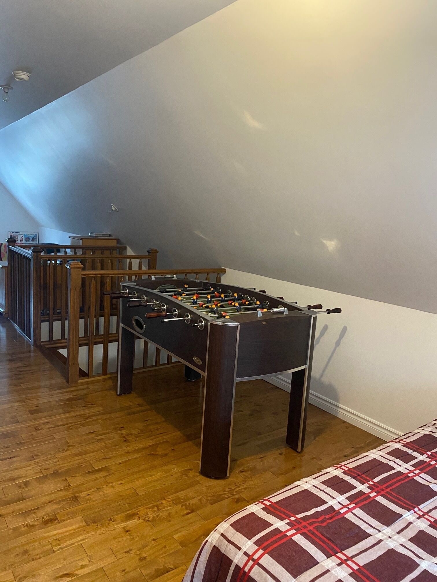 Ett rum med ett fotbollsspel, möbler i trä och ett mönstrat överkast.