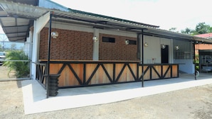 A building with a brick facade, a wooden deck, and a metal roof. - Asha Hostel (La Fortuna)