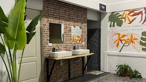 A bathroom with a brick wall, two sinks, a mirror, and a potted plant. - Asha Hostel (La Fortuna)
