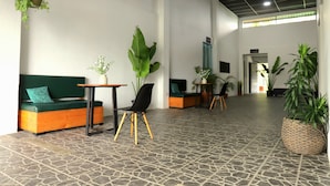 A spacious lobby with a stone-tiled floor, a green sofa, a black chair, and multiple potted plants. - Asha Hostel (La Fortuna)