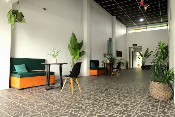 A spacious lobby with a stone-tiled floor, a green sofa, a black chair, and multiple potted plants. - Asha Hostel (La Fortuna)