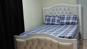Una cama con cabecera capitonada, colcha a cuadros y un equipo de aire acondicionado en la pared.