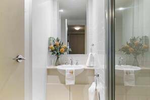 A bathroom with two sinks, a mirror, and a glass shower enclosure. - 1-bedroom Unit in Classic Melbourne CBD Building! (Melbourne)